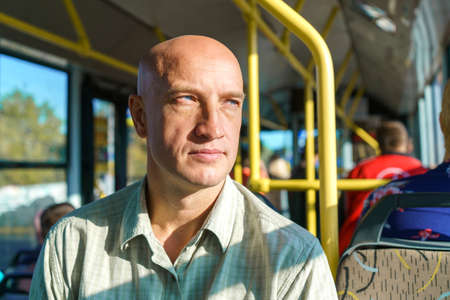 Bald caucasian man rides in public transport while sitting by the window on a sunny warm day. Enjoy the bus ride. Close-upの写真素材