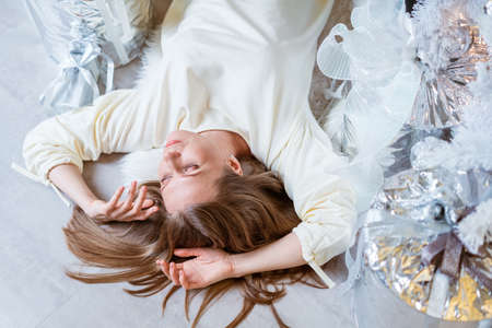 High angle view of caucasian beautiful woman lying on the floor near a christmas tree with gifts. Top view of happy girl resting and enjoying christmasの写真素材