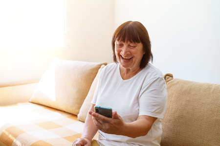 Happy mature 60s old woman holding smartphone with mobile phone app for video call, laughing while...