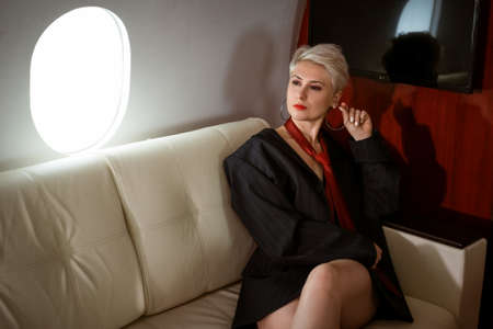Beautiful luxurious and sexy woman in a blazer and red tie on a private jetの写真素材