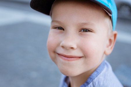 portrait of a little boy in a blue cap on the street close-up. A child with blonde hair and blue eyes looks at the camera and smiles against the background of a city street.の写真素材