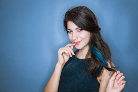 Image of a happy young lady standing isolated on a blue background. Looking camera holding finger to mouth and smiling cuteの写真素材