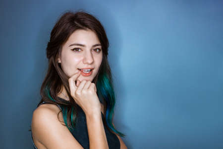 Surprised tender young woman of 20s holding finger at mouth open isolated on blue background studio portrait. With a mysterious pensive expression flirtsの写真素材