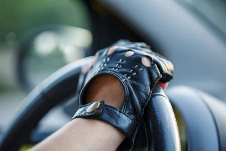 The drivers hands in leather gloves driving a moving car. Woman holding steering wheel in racing glovesの写真素材