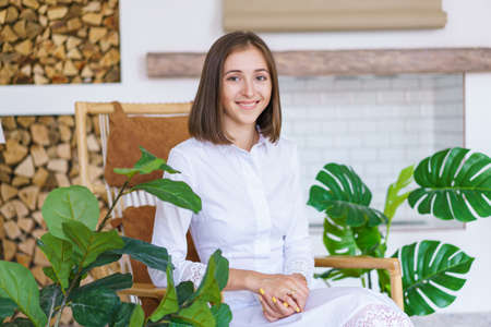 Successful young woman is sitting in chair and smiling and looking at camera. Enjoys leisure time in...
