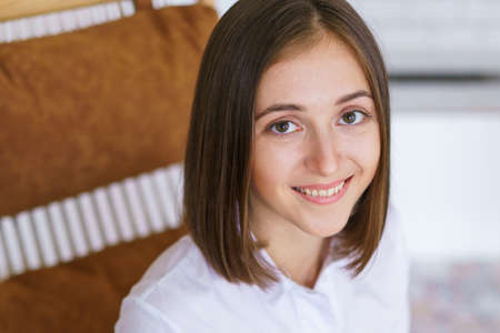 Successful young woman is sitting in chair and smiling and looking at camera. Enjoys leisure time in...