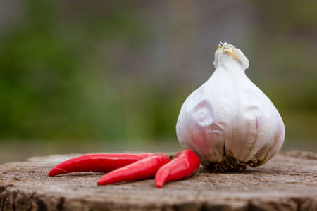 Head of garlic and red hot peppers on a wooden background close-up of a board with black peas. Selective focus and daylightの写真素材