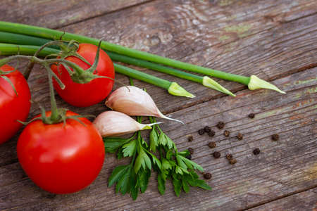 Red tomatoes green onions and garlic and parsley with black peas on a wooden background close-up with selective focus with soft light. Fresh homemade vegetablesの写真素材