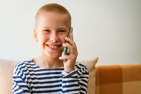 Happy little boy having fun playing game on mobile phone, preschool child sitting on sofa with...