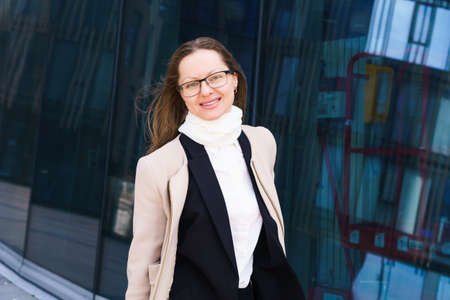 Portrait of a happy successful Caucasian ethnicity woman in glasses, stands in a coat and suit...