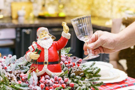 Beautiful christmas figurine of santa claus and decorative souvenirs with symbols of the new year on the table, a mans hand holds a glass. Christmas mood at the festive tableの写真素材