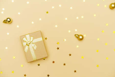 Christmas gift box with golden ribbon and bow on yellow background with christmas balls and candy stars, merry christmas and happy new year greeting cardの写真素材