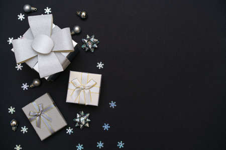 Christmas background from gift boxes of silver color, decorative snowflakes on dark black background. Festive christmas background. Banner layout, postcard. Flat lay. Copy space.の写真素材