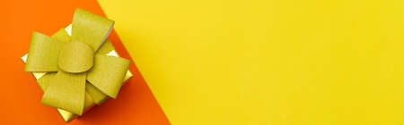 Bright yellow gift box with gold bow and ribbon on yellow and orange background. Flat lay festive background. Birthday gift, march 8, mothers day, valentines day. Christmas greetingsの写真素材
