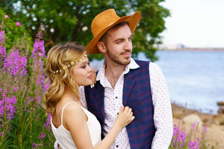 a young couple in love, a man and a woman, are walking in nature. the girl is a beautiful blonde with long hair in a white dress, the guy is dark in a white shirt, jacket and hat.の写真素材