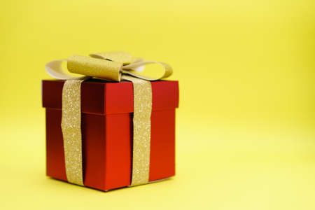 Red gift box with gold ribbon and bow on yellow background. Universal suitable for any occasion, be it birthday or christmasの写真素材