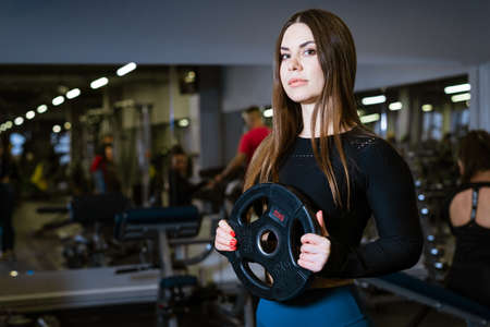 Determined and strong fitness woman exercising with heavy weights in fitness club. Sportswoman holding a heavy barbell in the gym. Caucasian girl in sportswear goes in for sportsの写真素材