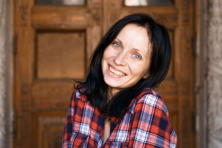Close-up face of pretty woman with blue eyes, natural dark hair, no makeup, standing in a plaid...