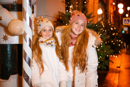 Lovely sisters teenagers walk on christmas eve along streets of evening city. Merry christmas and happy holidays. Family on a walkの写真素材