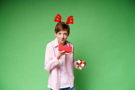 Shocked guy with deer antlers holding gift box on green background, copy space. Surprised boy in...