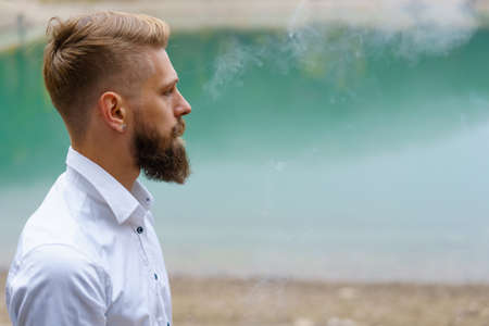 Young man beard smokes cigarette or tobacco. Guy is addicted to cigarettes and always smokes lot of...