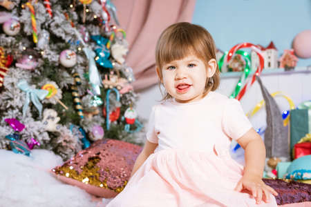 portrait of a small blonde baby girl playing near the Christmas tree. the child is wearing a white T-shirt and a pink skirt. Holiday Conceptの写真素材
