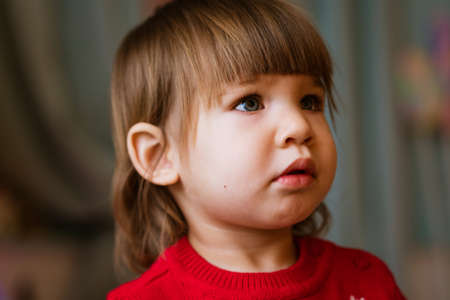 Child close-up portrait of little girl in red sweater. Waiting to receive presents for christmas and...
