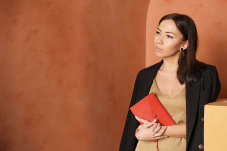 Close-up view of woman wearing black jacket and holding book with an empty red cover. Free space for...