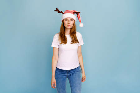 Studio portrait of young woman with long hair wearing a close hat of santa claus with antlers and in white t-shirt on blue background cute smiling. Close up, copy space for text, isolated background.の写真素材