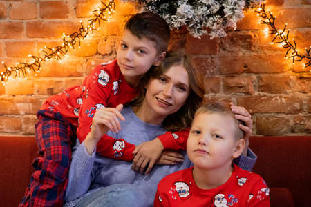 Happy family mother with sons on christmas morning in pajamas near christmas tree with gifts. Caucasian happy family for new yearの写真素材