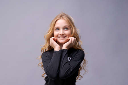 Photo of dreamy cute positive little girl with blond long wavy hair looking blank space wonder smile in black clothes isolated on light gray backgroundの写真素材