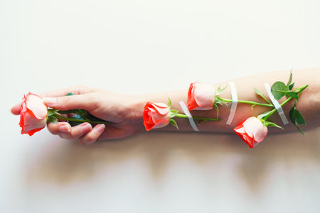 Women fashion hands of natural cosmetics, red roses, beautiful flowers and thorns glued with adhesive plaster, hand care. Womens health problems, girl studio shot light backgroundの写真素材