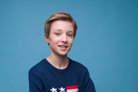 Happy relaxed contented handsome young man standing in blue sweater with usa flag celebrating national day, posing in studio. Isolated on blue background.の写真素材