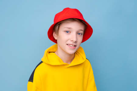 Rapper. City style. Model shooting. Happy hipster guy in yellow sweatshirt and red hat isolated blue...