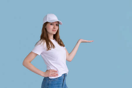 Young happy surprised smiling female promoter 20s in white casual t-shirt and cap pointing with hand...