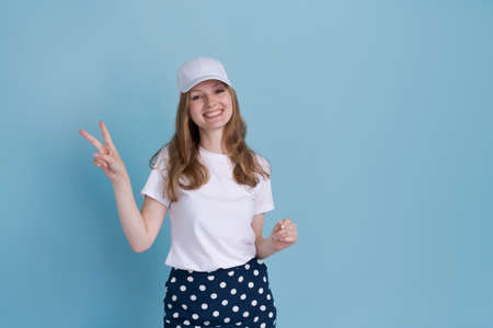 Excited young caucasian woman pointing aside at copy space on blue background with hand in white...