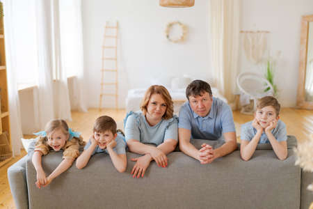 Big happy family posing near new purchased sofa in bright living room at home. Happiness and joy in a house with many children. Everyone is smiling and looking at the cameraの写真素材