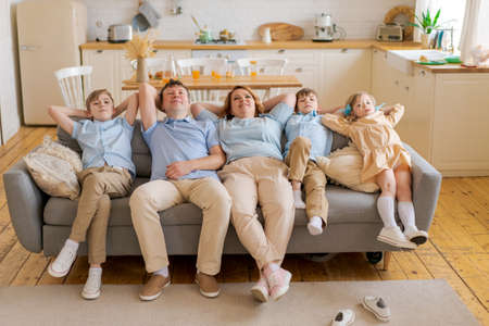 Big cute beautiful adorable receptionist cute cheerful excited caucasian family in casual clothes, five people, cute mom, happy dad, three children sitting in the living room, light color interiorの写真素材