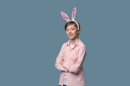 A young guy in pink shirt with easter bunny ears on his head poses cheerfully and gesticulates with...