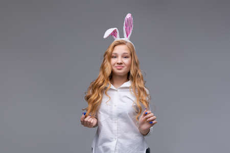 Young beautiful woman in cute easter bunny ears makes a normal gesture, plays with her hand with...