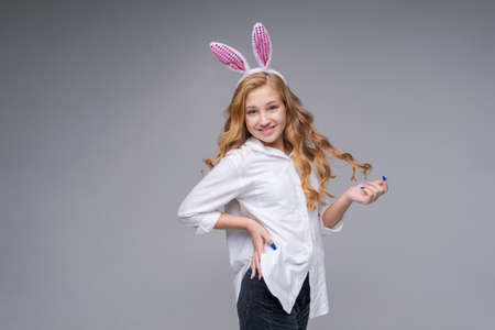 Young beautiful woman in cute easter bunny ears makes a normal gesture, plays with her hand with...