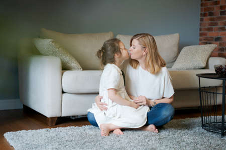 Smiling senior caucasian grandmother and little girl are relaxing at home together sitting on floor by couch, hugging and playing. Happy mature woman hugs her little granddaughter. Family concept.の写真素材