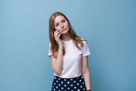 Excited young caucasian woman making or answering phone call, standing isolated over blue studio...