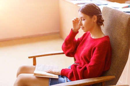 Free time for rest. Young calm caucasian woman sits in comfortable chair and reads paper book in a...