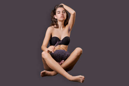 Girl in shorts sticks out them lavender like pubic hair. Symbol stubble and problems with home depilation. Razor near excess hair. Body positivity and body hair problems. On a black backgroundの写真素材