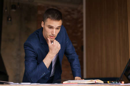 Serious caucasian businessman accountant accounting analyst holding documents looking at computer...