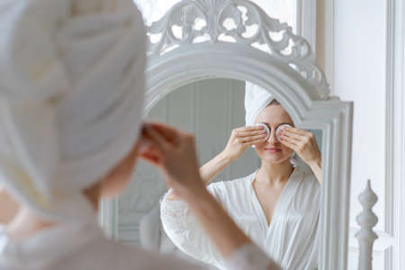 Happy female cleansing skin with cotton pads in bathroom, attractive caucasian woman doing morning...