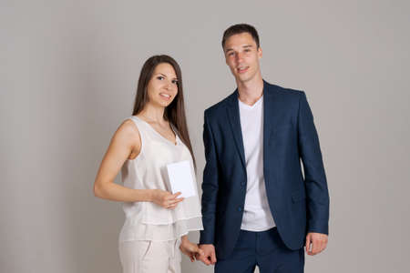 Business partner gives certificate to happy woman on gray background. Caucasian couple in business clothes, man gives beautiful girl a blank about winning the competition on a gray studio backgroundの写真素材