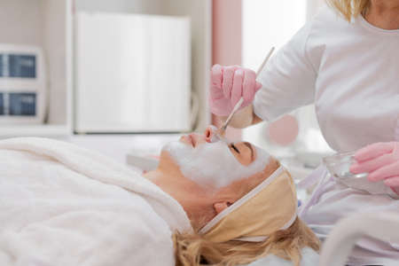 Female cosmetologist makes facial procedures for client clinic in aesthetic medicine. Beautician or dermatologist makes a peeling or lifting massage to a woman in a spa or salon. Selective focusの写真素材