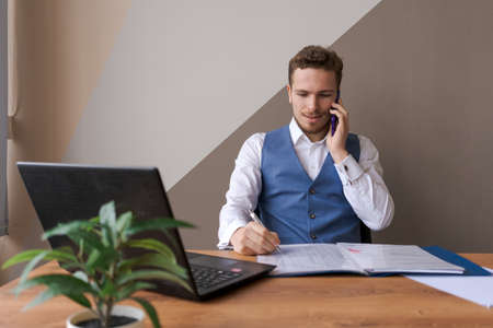 Portrait successful businessman with beard using smartphone and working on documents in office,...